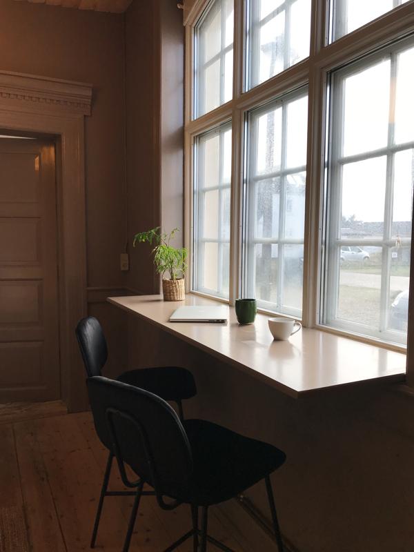 Arbejdsplads ved de store sprossede vinduer med bærbar, kaffekop og plante